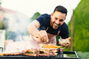 Smiling man seasoning meat on the grill